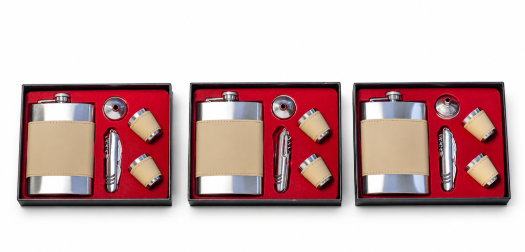 Beige-wrapped silver-tone hip flask, two cups, funnel and folding pocket tool in red-lined presentation boxes on a white background